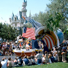 photo of Disneyland attraction America On Parade featuring life-size Mickey Mouse, Donald Duck, and Goofy all marching on moving float beneath large American flag