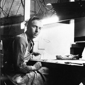 black and white photo of a young Walt Disney at workbench wearing a full-length apron