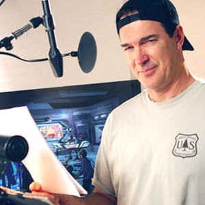 photo of Patrick Warburton in recording studio behind microphone holding script