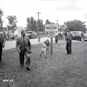 photo of Walt Disney walking across grass beside city limits sign for Marceline Missouri in 1956