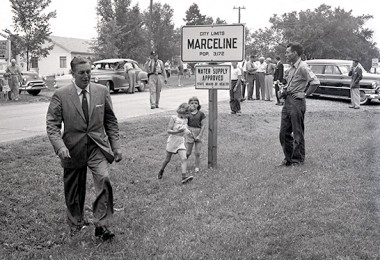 photo of Walt Disney walking across grass beside city limits sign for Marceline Missouri in 1956
