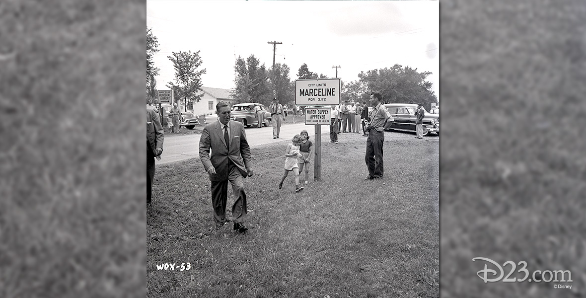 photo of Walt Disney walking across grass beside city limits sign for Marceline Missouri in 1956