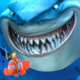 animation still from the feature Finding Nemo showing a giant grinning shark looming behind the minuscule Nemo