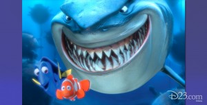animation still from the feature Finding Nemo showing a giant grinning shark looming behind the minuscule Nemo