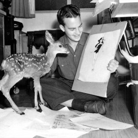 photo of Bill Justice sitting on floor holding a recent sketch in one hand and a live doe in the other