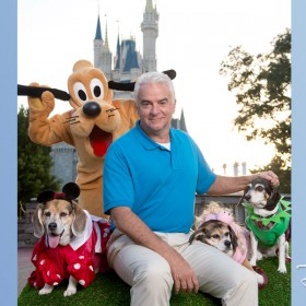 photo of host seated with Goofy character and two dogs in costume from America's Cutest: Disney Side Howl-0-Ween