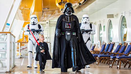 photo of Darth Vader marching along deck of cruise liner followed by two Stormtroopers with a small boy holding a light saber toy beside him