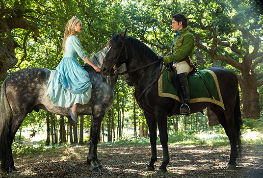 still from the movie Cinderella featuring Lily James as Ella and Richard Madden as Prince "Kit" Charming meeting on horseback in bright forest