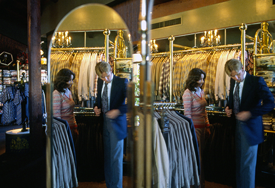 photo of sales agent assisting buyer trying on jacket reflected in full-size image