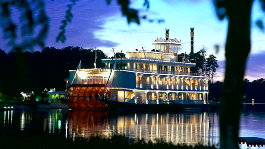 sunset photo of glamorous brightly lit riverboat with lights reflected across the lake