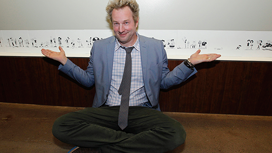 photo of Tom Warburton, Co-Executive Producer, The 7D, seated in front of wall displaying his very wide pen and ink drawing