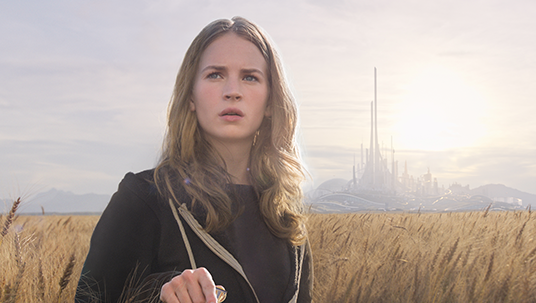 still from the movie Tomorrowland featuring actress Britt Robertson standing in a wheat field with the spires of Tomorrowland in the distance behind her