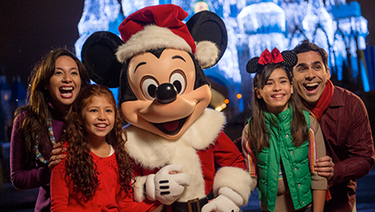 photo of smiling family huddled together with Mickey Mouse costumed character wearing santa clause fur-lined coat and cap