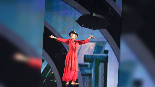 photo of Kym Johnson as Mary Poppins floating over stage with open umbrella held in outstretched hand