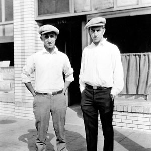 black and white photo of Roy and Walt Disney wearing caps standing in front of empty storefront