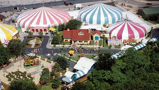 This birds-eye view of Mickey’s Birthdayland showcases the general layout of the area. Note Mickey’s house at center (complete with car parked in the driveway), and the several small Duckburg-themed facades near the front sides of the larger show tents. Weather eyes can spot Cornelius Coot Commons at the top left. This small square and fountain was dedicated to the founder of Duckburg, U.S.A., Cornelius Coot.