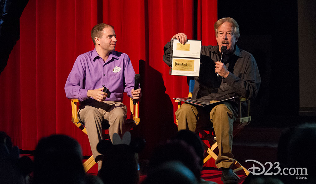 D23’s Steven Vagnini and Disney Legend Tony Baxter show the audience a gold-colored ticket.