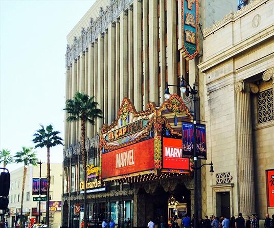 daytime photo of exterior of El Capitan Theatre showing bright red-backed Marvel Studios logo on marquee