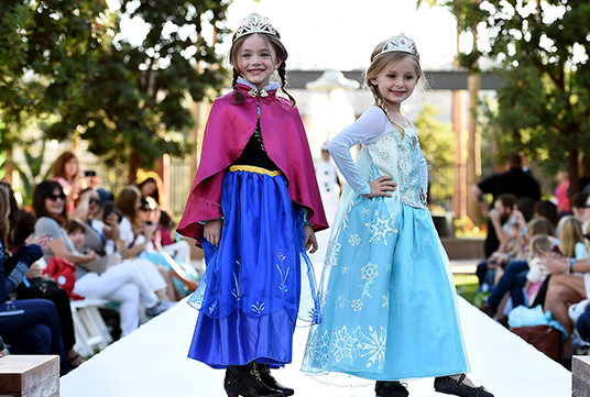photo of two young girls in princess garb standing on an outdoor fashion catwalk