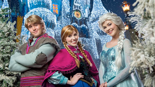 photo of actors dressed as Kristoff, Anna and Elsa from the movie Frozen standing in front of projection of ice crystal-laden frozen Sleeping Beauty Castle