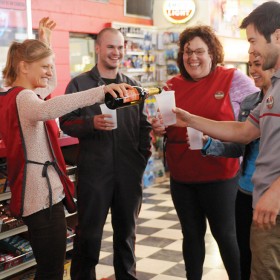 production group photo of four characters toasting each other with plastic cups