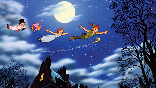 scene from animated feature Peter Pan showing Peter Pan and three children flying over rooftops at night under a bright full moon