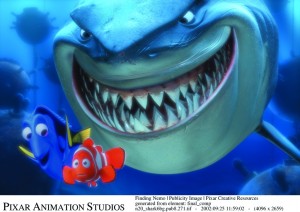 animation still from the feature Finding Nemo showing a giant grinning shark looming behind the minuscule Nemo