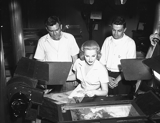 black and white photo of Mary Costa and Sleeping Beauty animators at huge animation camera stand with cel in place for photographing