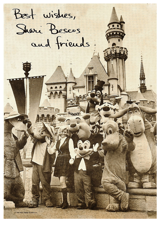 black and white photo showing Shari Bescos posing with Mickey Mouse, Pluto and friends in front of Sleeping Beauty Castle at Disneyland
