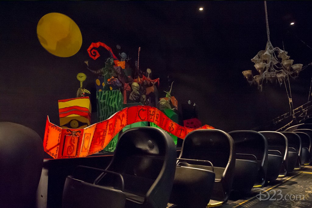 photo of portion of Haunted Mansion ride showing string of empty ride cars beside bright red Scary Christmas banner