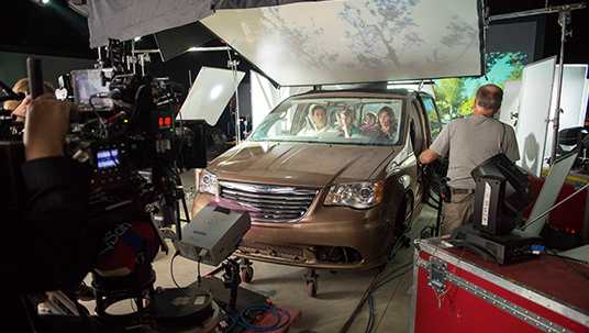 behind the scenes photo from set of Alexander and the Terrible, Horrible, No Good, Very Bad Day showing Jennifer Garner, Steve Carell and cast in a car scene being readied for filming a scene inside a studio with lights and cameras and technicians all around
