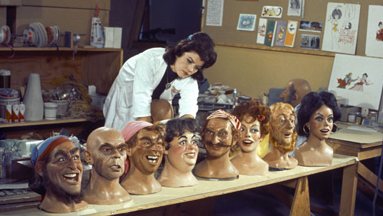 photo of Imagineer Leota Toombs, Madame Leota's face and namesake from the Haunted Mansion attraction, with busts from an assortment of characters from Disneyland attractions including Pirates of the Caribbean