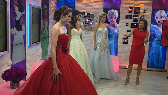 three ladies in long formal gowns being judged by a fourth lady show hostess