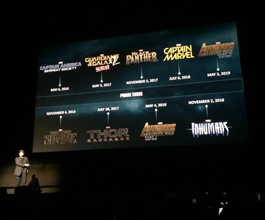 photo of Marvel Studios' president Kevin Feige on stage at Hollywood's El Capitan Theatre showing projected titles of Marvel movies current and planned