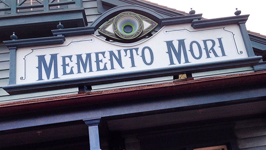 photo of exterior sign above Memento Mori shop that features Haunted Mansion-themed merchandise
