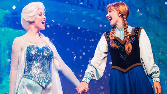 photo of singers in costumes as Elsa and Anna from Frozen holding hands singing