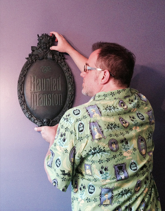 photo of Brian Frey hanging a egg-shaped placard replica of The Haunted Mansion front sign