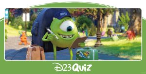 Mike Wazowski, a green, one-eyed monster from Monsters University, is looking at his check list in one hand and has a pen in his other hand while standing on a college campus walk path with green grass on either side of the path. He is wearing a dark blue hat that has "MU" written on the front of it while wearing a dark blue backpack with a tan suitcase and a green suitcase, both featuring stickers, on either side of him.