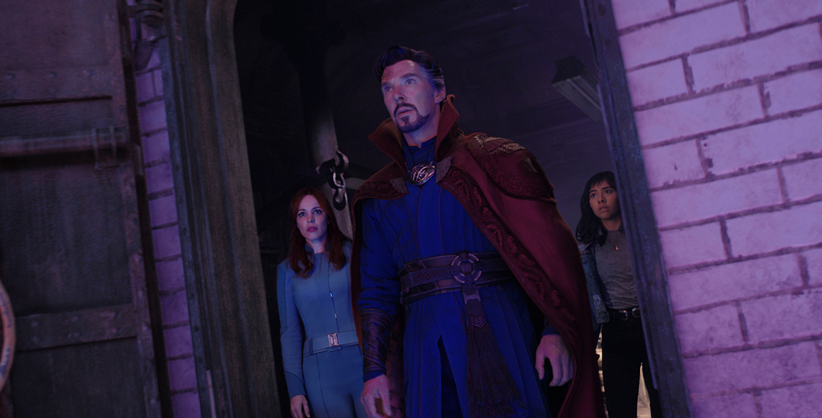 Christine Palmer, Doctor Strange, and America Chavez stand in a door, cast in purple-hued light. They all are staring in surprise at something just off camera.