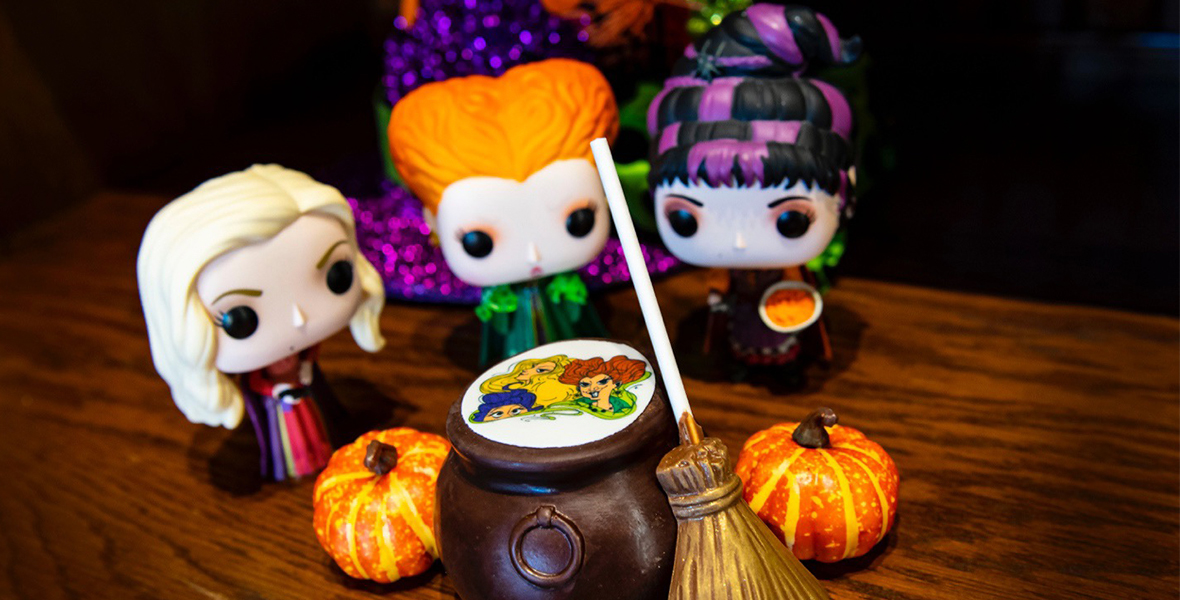 The Sister’s Elixir Hot Cocoa Bomb, surrounded by Halloween decorations and the three Funko Pops of the Sanderson sisters.