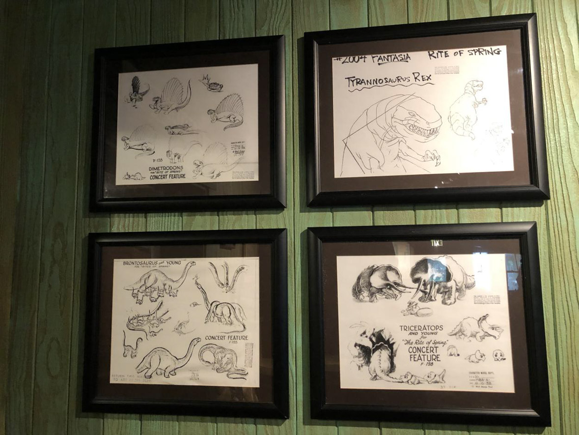 Four framed concept art of dinosaurs on the wall,