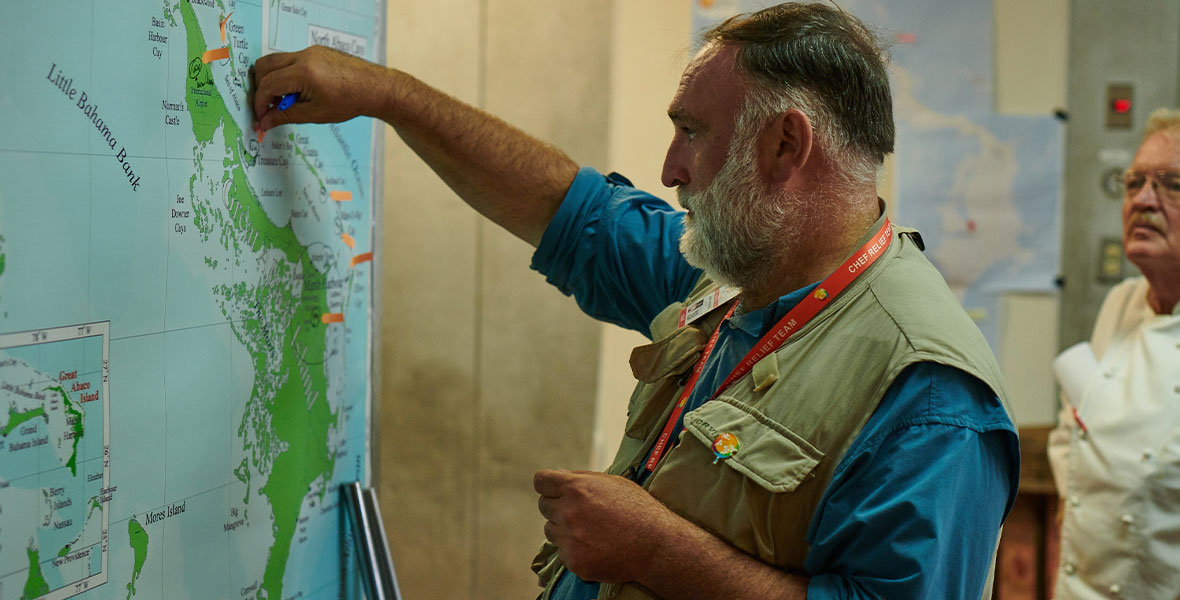 In the Disney+ show We Feed People, a man is standing in front of a large map and marking locations with orange arrow shaped sticky notes.