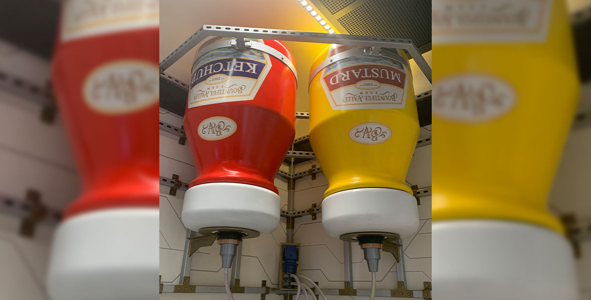 A super-sized ketchup and mustard bottle inside the Pym Test Kitchen, featuring a label depicting the “Bountiful Valley Farms” logo.