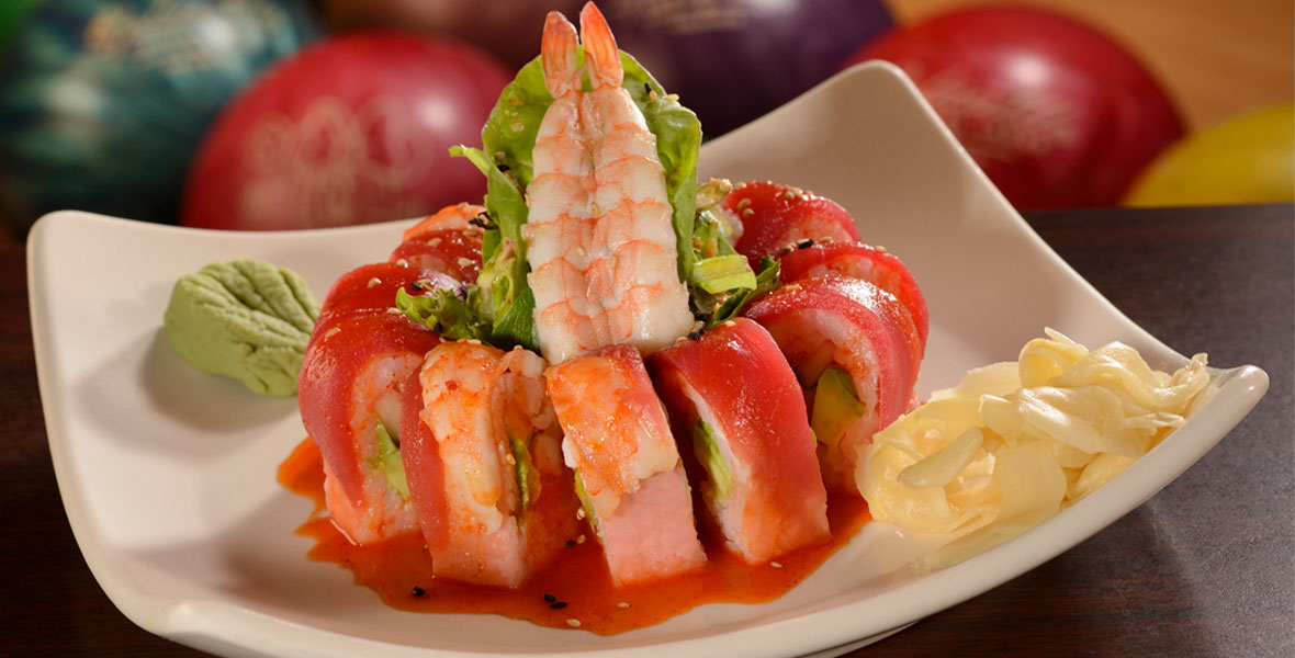 An image of the Galaxy sushi roll from Splitsville Luxury Lanes—which includes salmon, cucumber, and avocado rolled in soy paper and topped with steamed shrimp and ahi tuna—set against a background of colorful bowling balls.