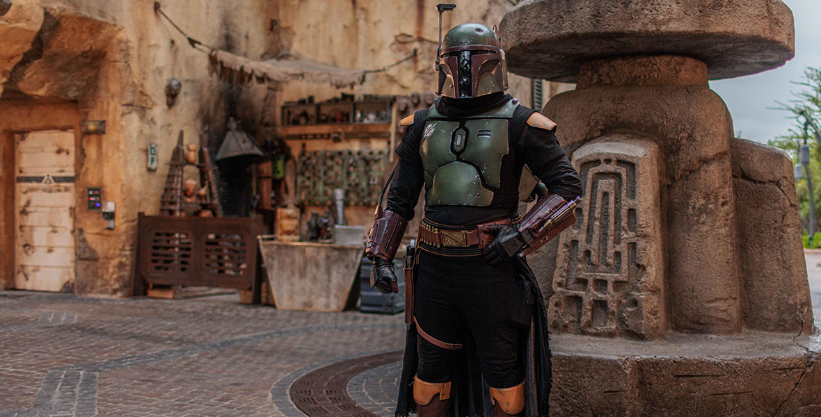 Boba Fett, in full armor, stands inside the Star Wars: Galaxy’s Edge marketplace.