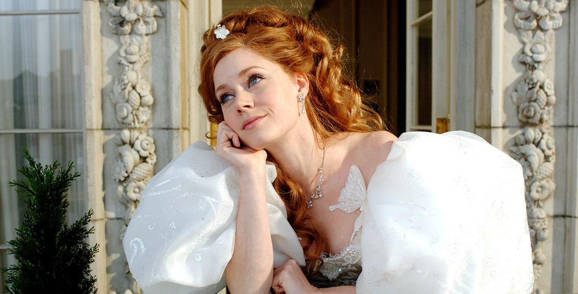 Actress Amy Adams, who is wearing a white wedding dress with big puffy sleeves, looks on from a balcony in New York City in the Disney film Enchanted. 