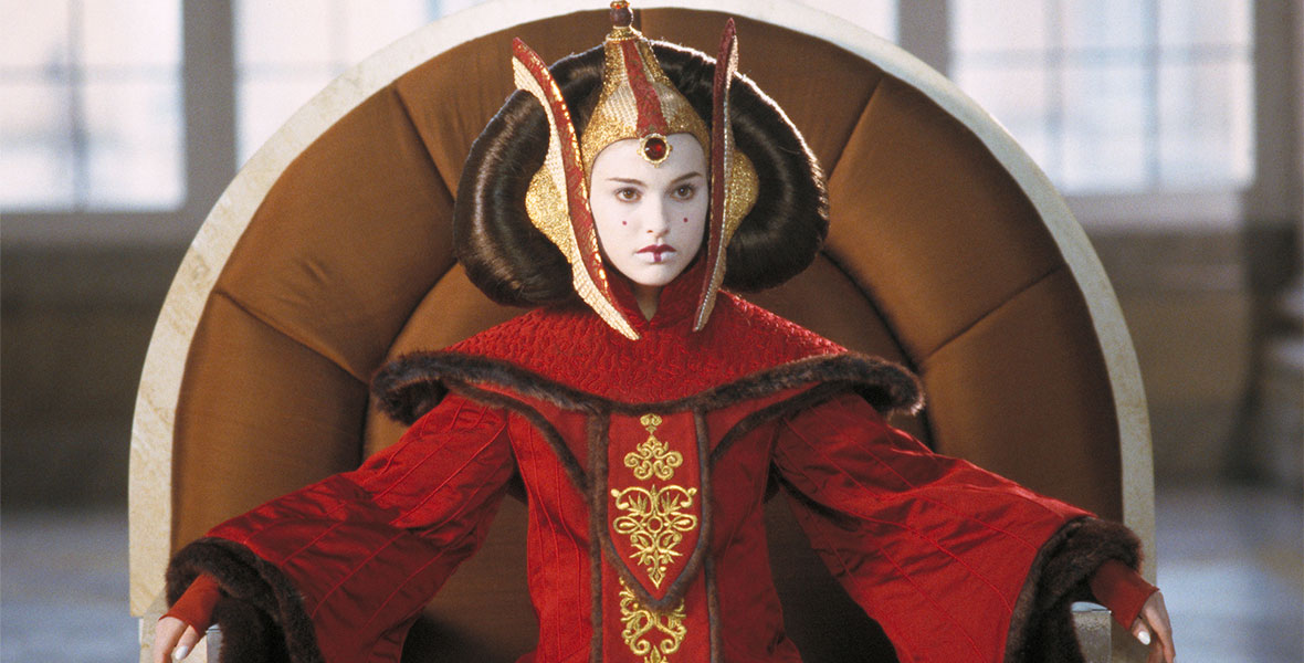 Queen Padmé Amidala sits on her throne with a serious expression. She wears a bright red gown and dramatic headpiece and hairstyle.