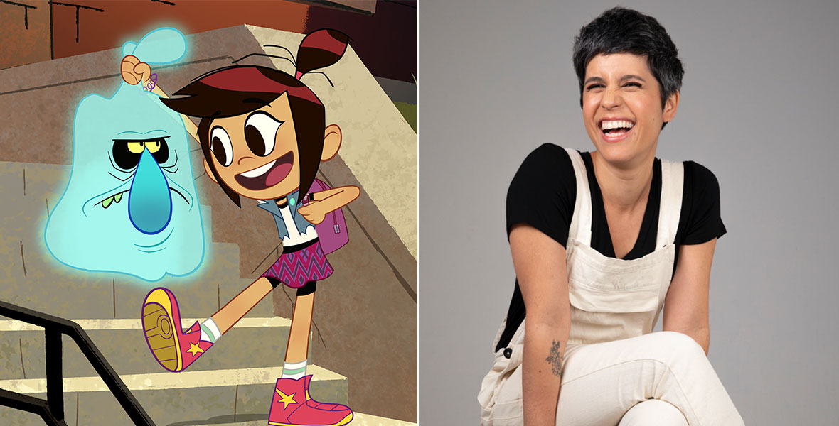 Ashly Burch laughs while sitting on a wooden stool in a pair of white overalls and a black shirt.
