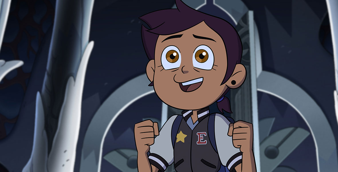 Luz (voiced by Sarah-Nicole Robles) stands excitedly inside large metal doors in the season finale of the animated series The Owl House.