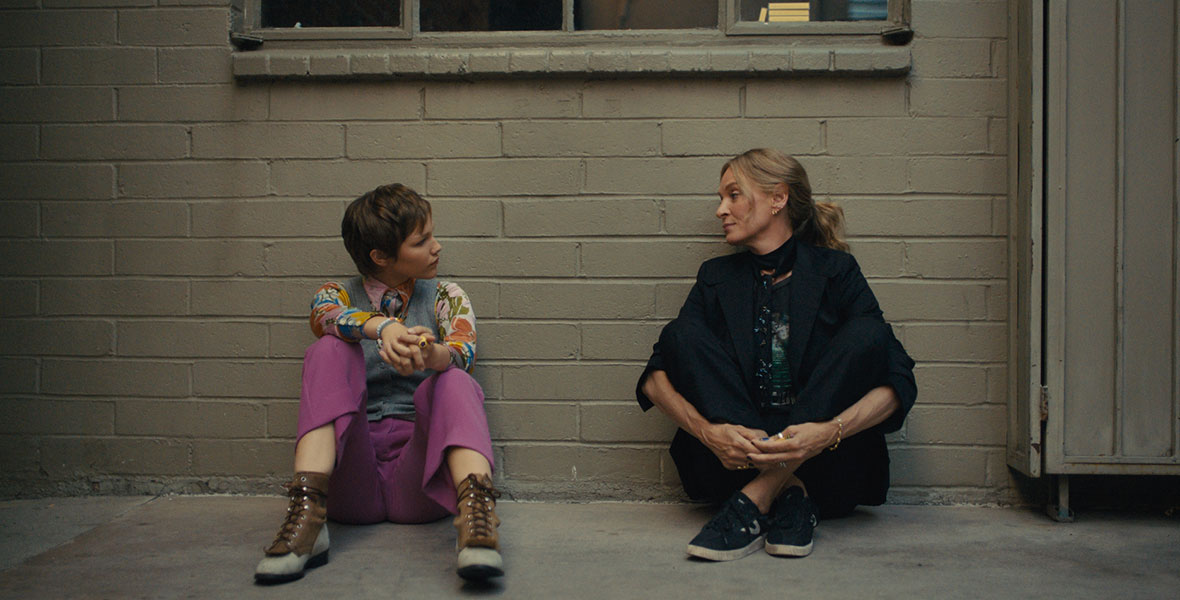 (L-R) Grace VanderWaal as Stargirl Caraway and Uma Thurman as Roxanne Martel in Disney+’s live-action film Hollywood Stargirl talk as they sit against a wall outside a recording studio.